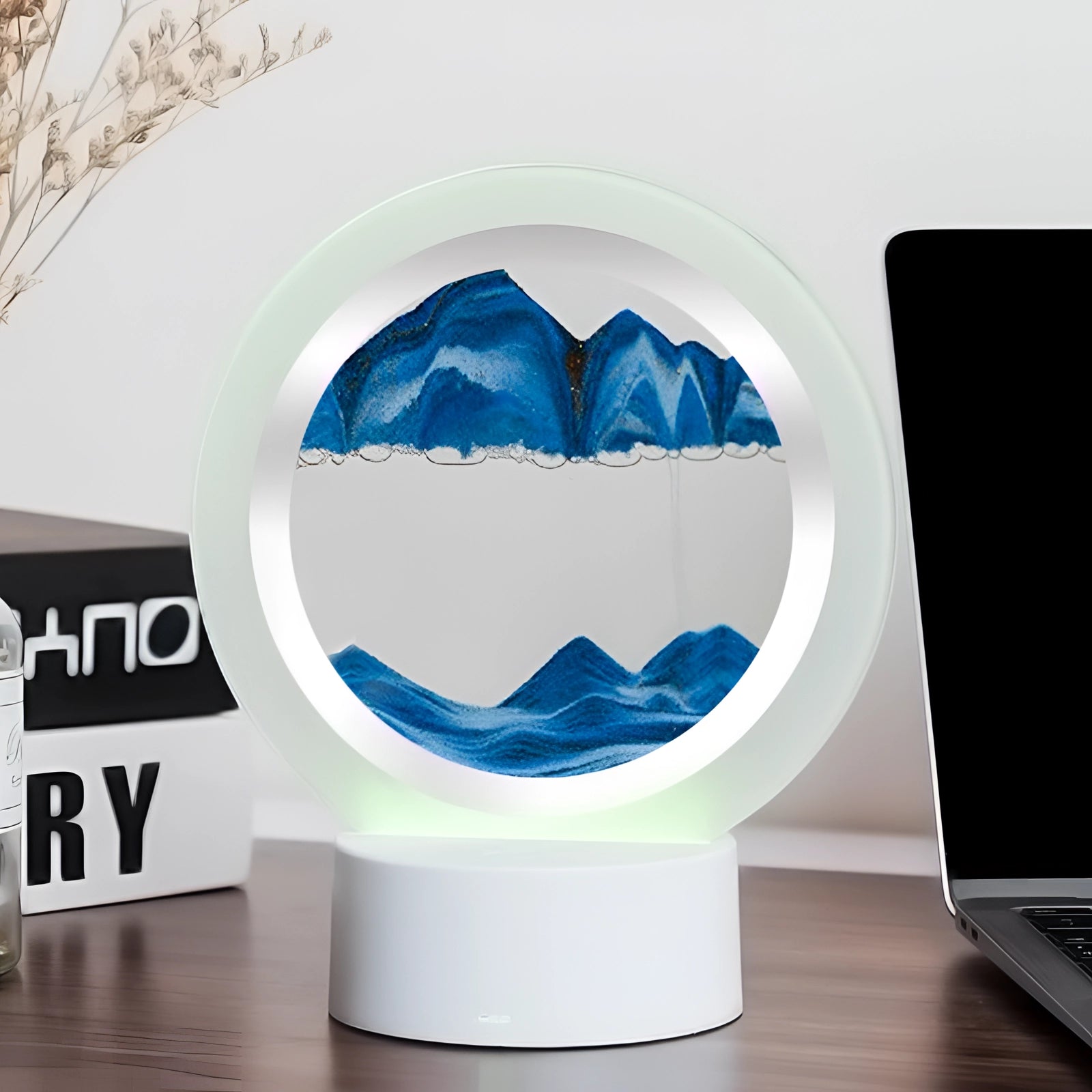 3D LED sand art night light lamp featuring a resin mountain design in blue, placed on a shelf near a laptop and keyboard.