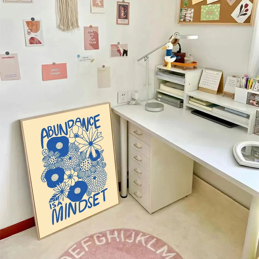 Blue and yellow floral art motivational poster with the phrase "Abundance Mindset" displayed in a stylish font, surrounded by an interior setting that includes wooden cabinetry, shelving, and a table.