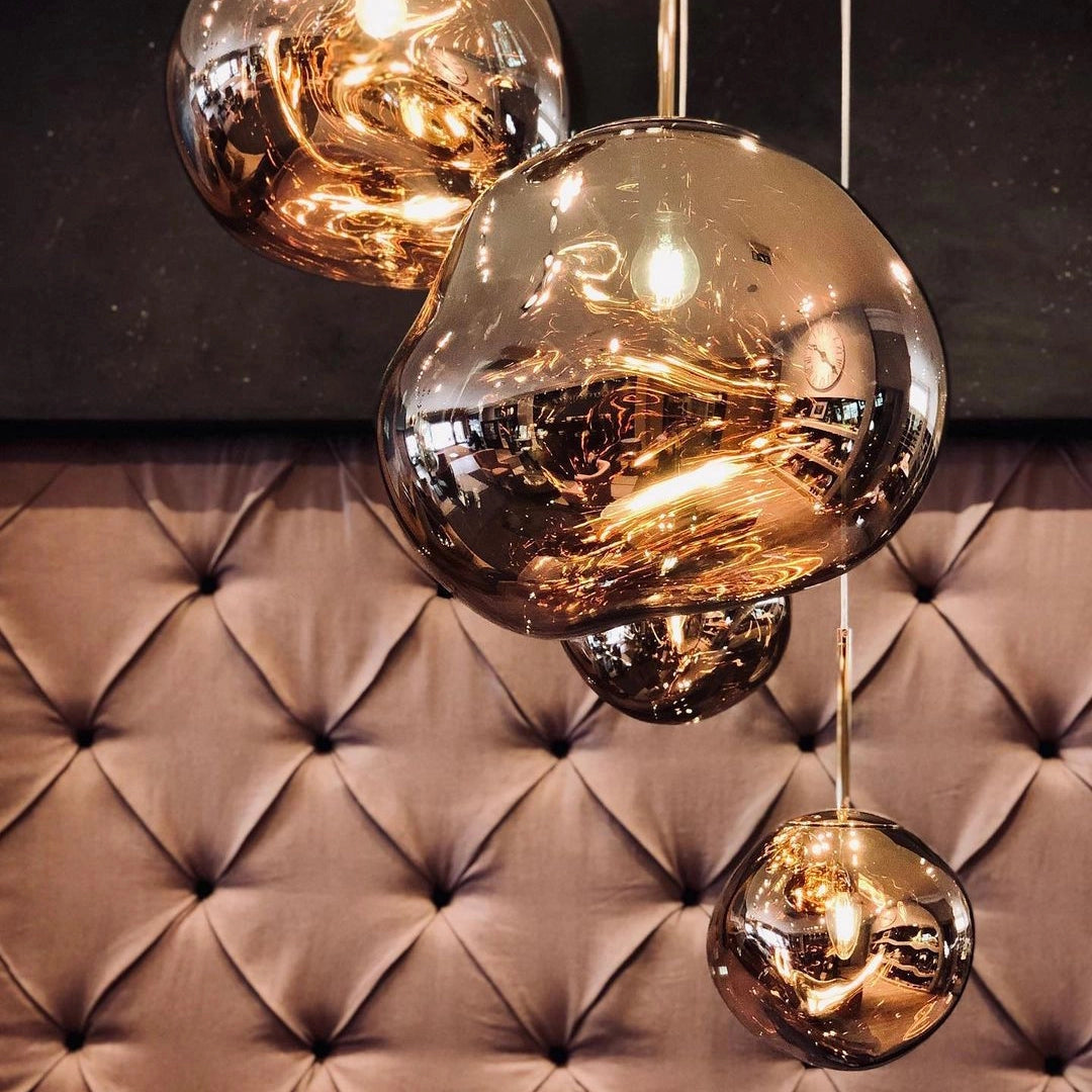 Amber glass triple pendant light fixture with a modern copper finish, featuring three spherical amber-tinted glass shades suspended in a linear arrangement, illuminating the space with a warm golden glow.