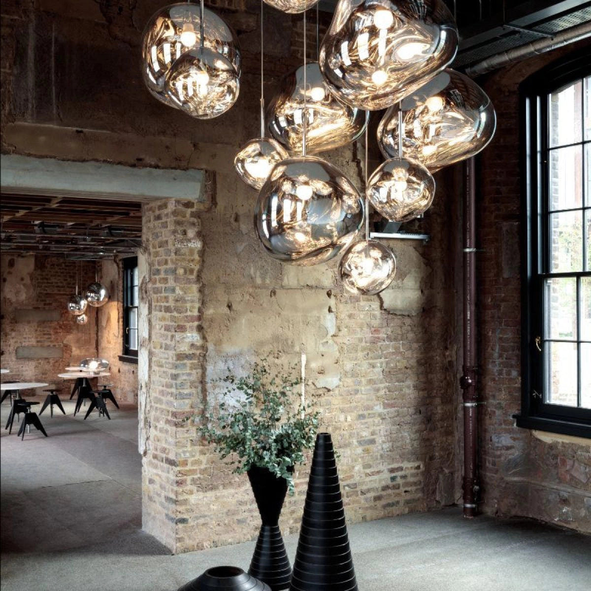 Amber glass triple pendant light fixture with modern copper accents hanging from the ceiling in a stylish interior space, complemented by natural light streaming through a large window and wooden furniture elements, including a table and chairs.