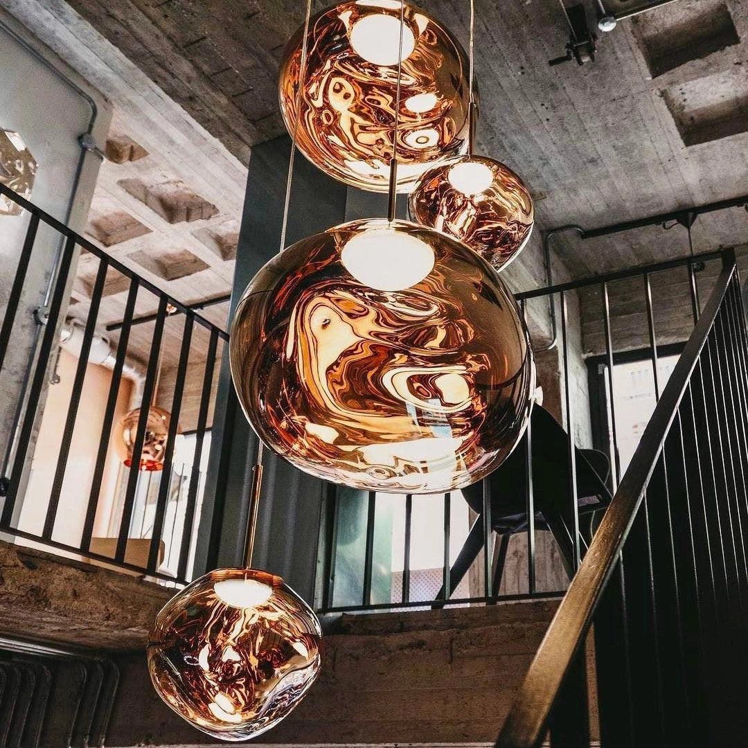 Amber glass triple pendant light fixture with a modern copper finish, featuring three symmetrical glass shades suspended from a circular ceiling mount, casting a warm amber glow.