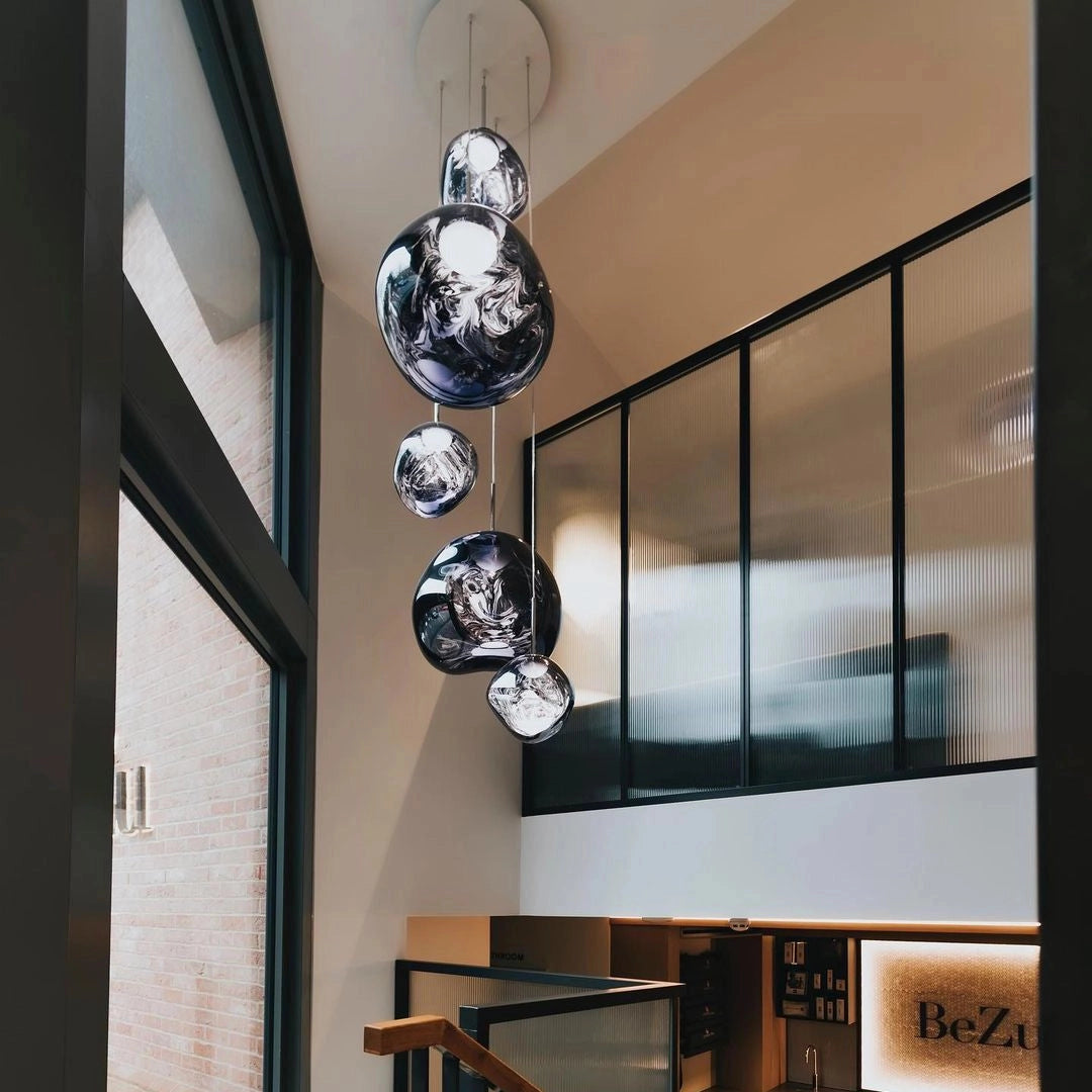 Amber glass triple pendant light fixture with modern copper accents, hanging from a ceiling in a stylishly designed interior space with wooden flooring and artistic elements.