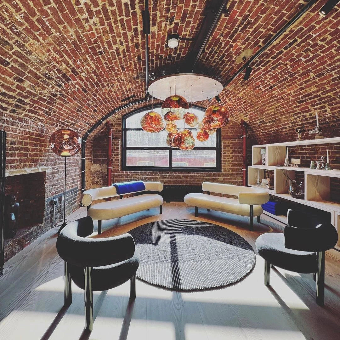 A modern copper ceiling lamp featuring an amber glass triple pendant light fixture, elegantly illuminating a stylish living room with contemporary furniture and brick accents.