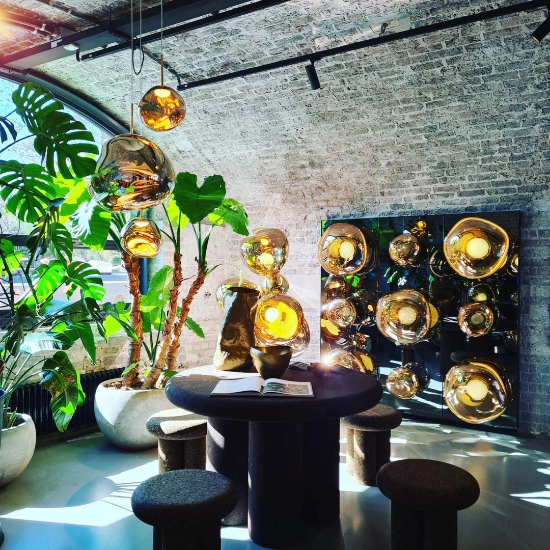 Amber glass triple pendant light fixture with modern copper accents, hanging above a decorative indoor plant in a contemporary interior space with stylish design elements.