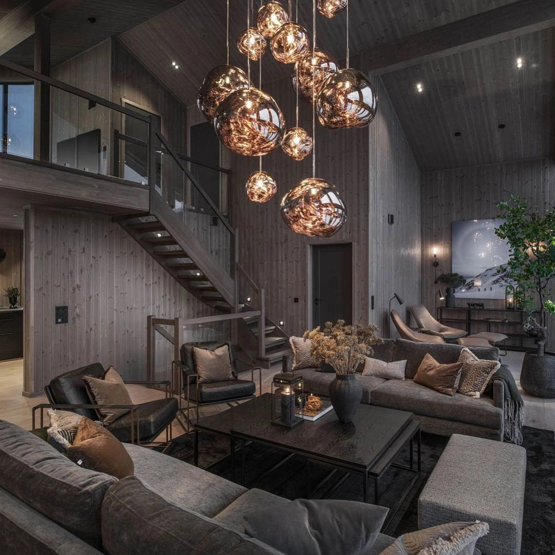 Modern interior featuring an amber glass triple pendant light fixture with copper accents hanging from the ceiling, illuminating a stylish room with a wooden table, a comfortable couch, and various indoor plants, creating a warm and inviting atmosphere.