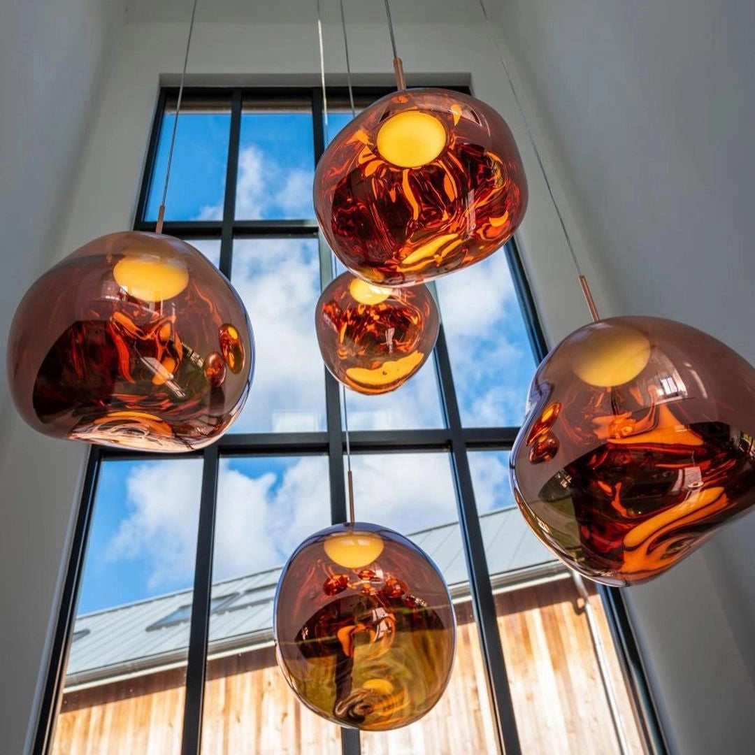 Amber glass triple pendant light fixture with modern copper accents, featuring three amber-tinted glass shades suspended from a sleek ceiling mount, casting a warm orange and yellow glow.