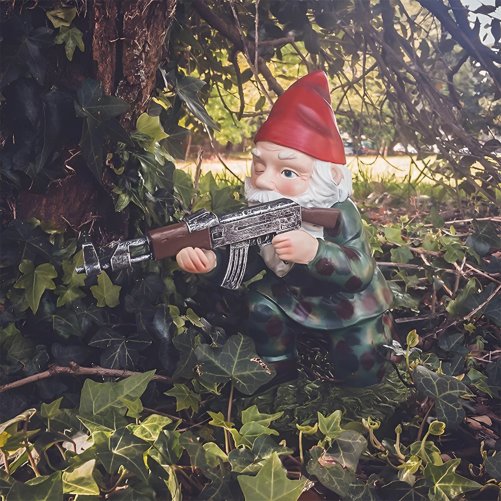 Armed warrior garden gnome statue dressed in military camouflage with an AK-47, standing on grass.
