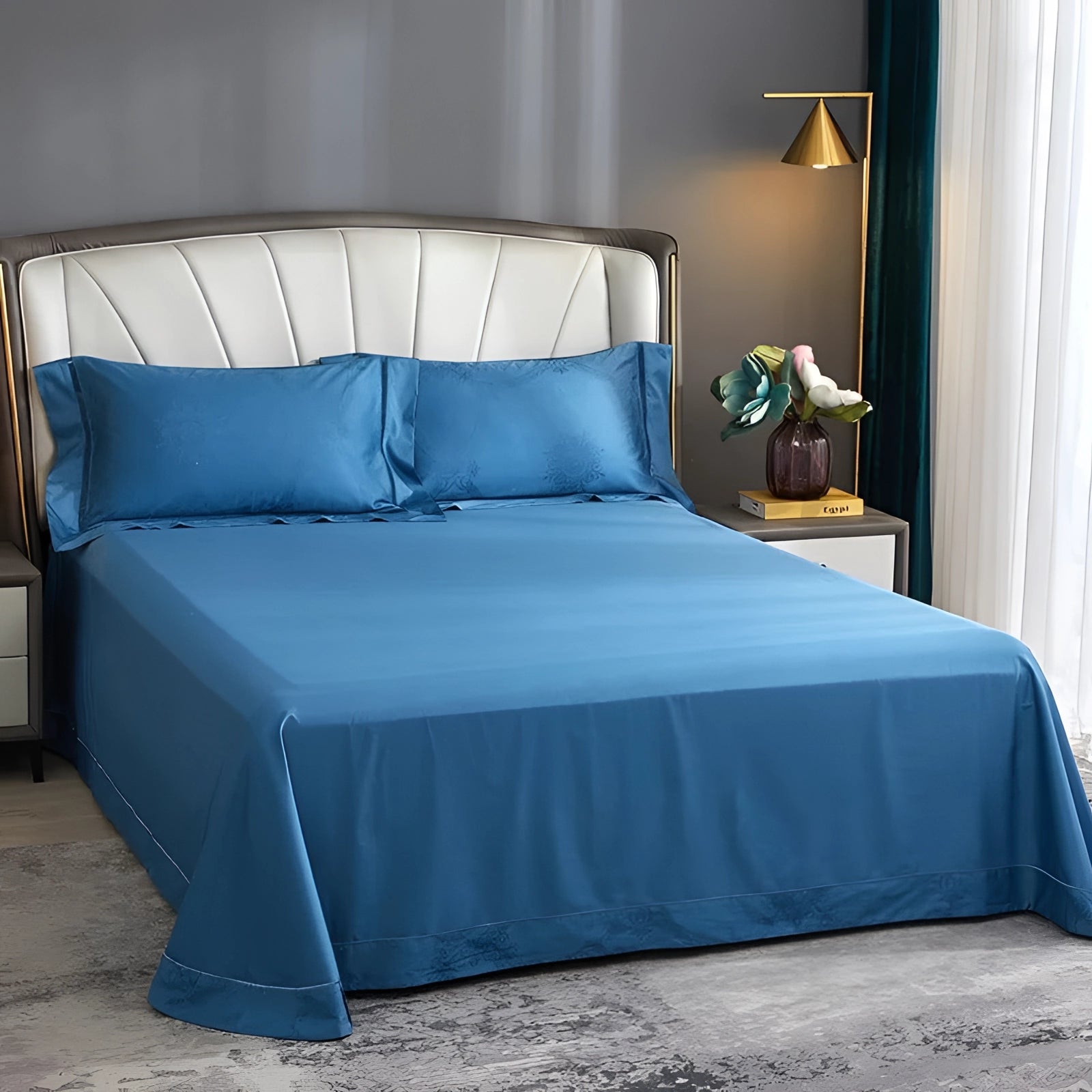 Blue king size silk bedsheet set with matching pillowcases on a wooden bed frame in a well-furnished bedroom featuring azure color scheme, wrinkle-free and hypoallergenic. Interior includes wooden flooring, walls, and curtains.