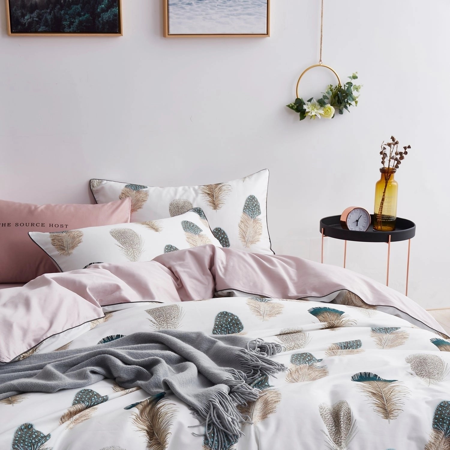 Botanical print feather pattern duvet set in pink and white on a neatly made bed, surrounded by a cozy interior with wooden furniture, a plant, and a picture frame.