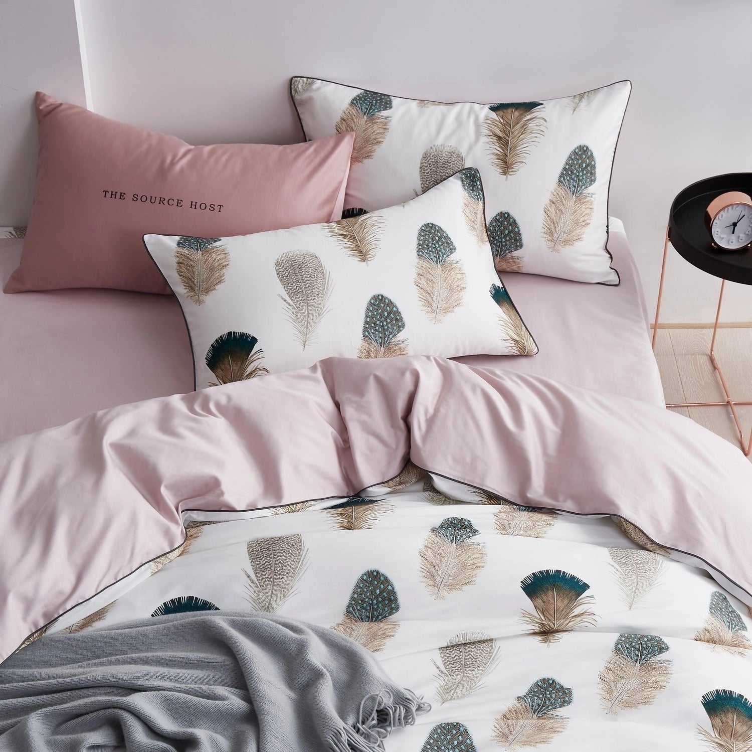 Pink and white luxury duvet set featuring a botanical print with feather patterns, accompanied by matching pillowcases, displayed on a bed.