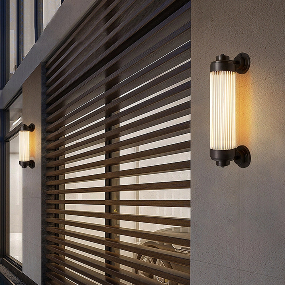 Bronze Vintage Glass Tube Wall Sconce featuring an industrial design, with an 18.9'' length, mounted on a wooden wall. The fixture has a glass tube shade and a bronze finish, ideal for adding a vintage touch to a bathroom or any interior space.