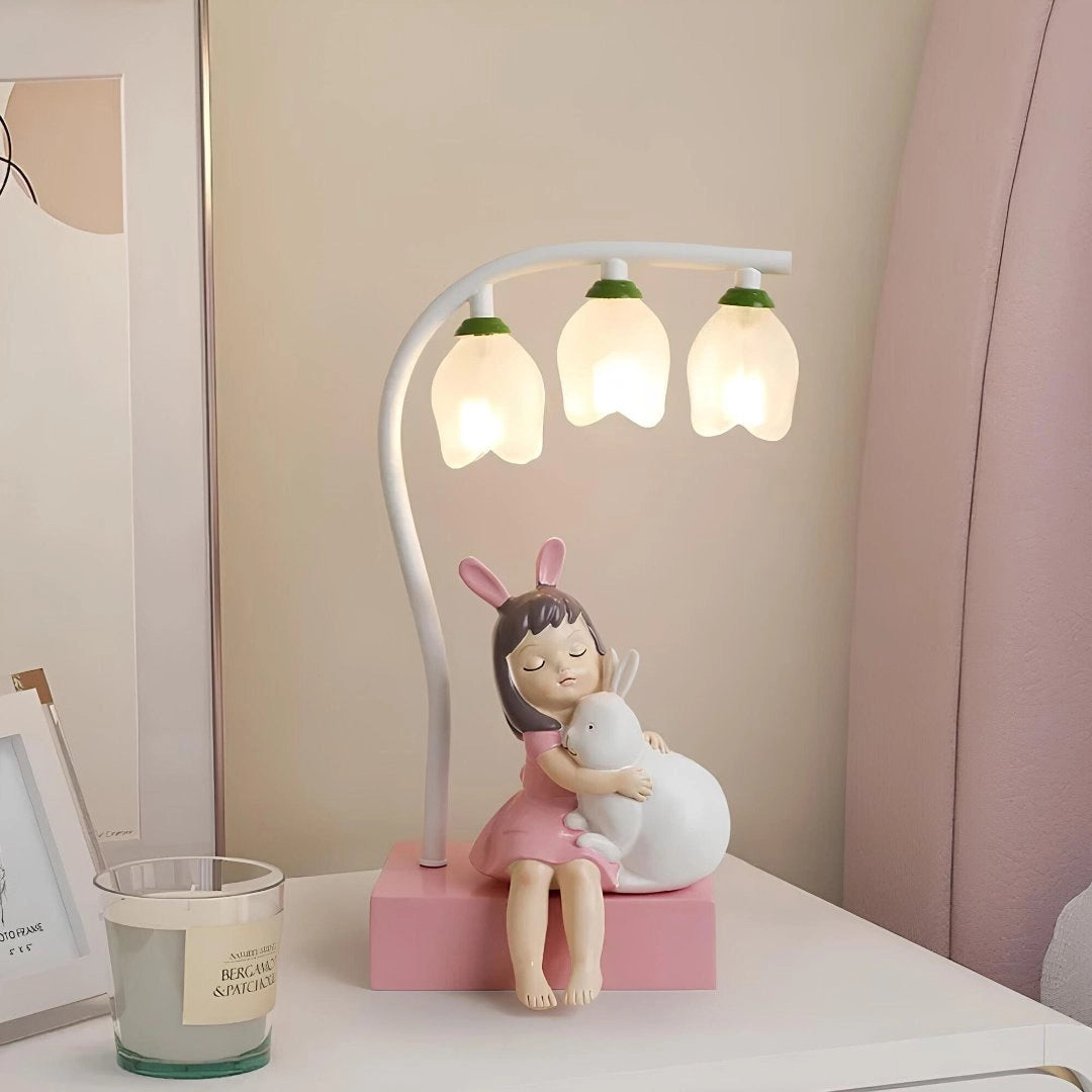 Cartoon bee-themed LED night light in pink, designed for kids, sitting on a table. The lamp has a cute and happy appearance, providing comfort and artful charm as a household accessory in a room setting.