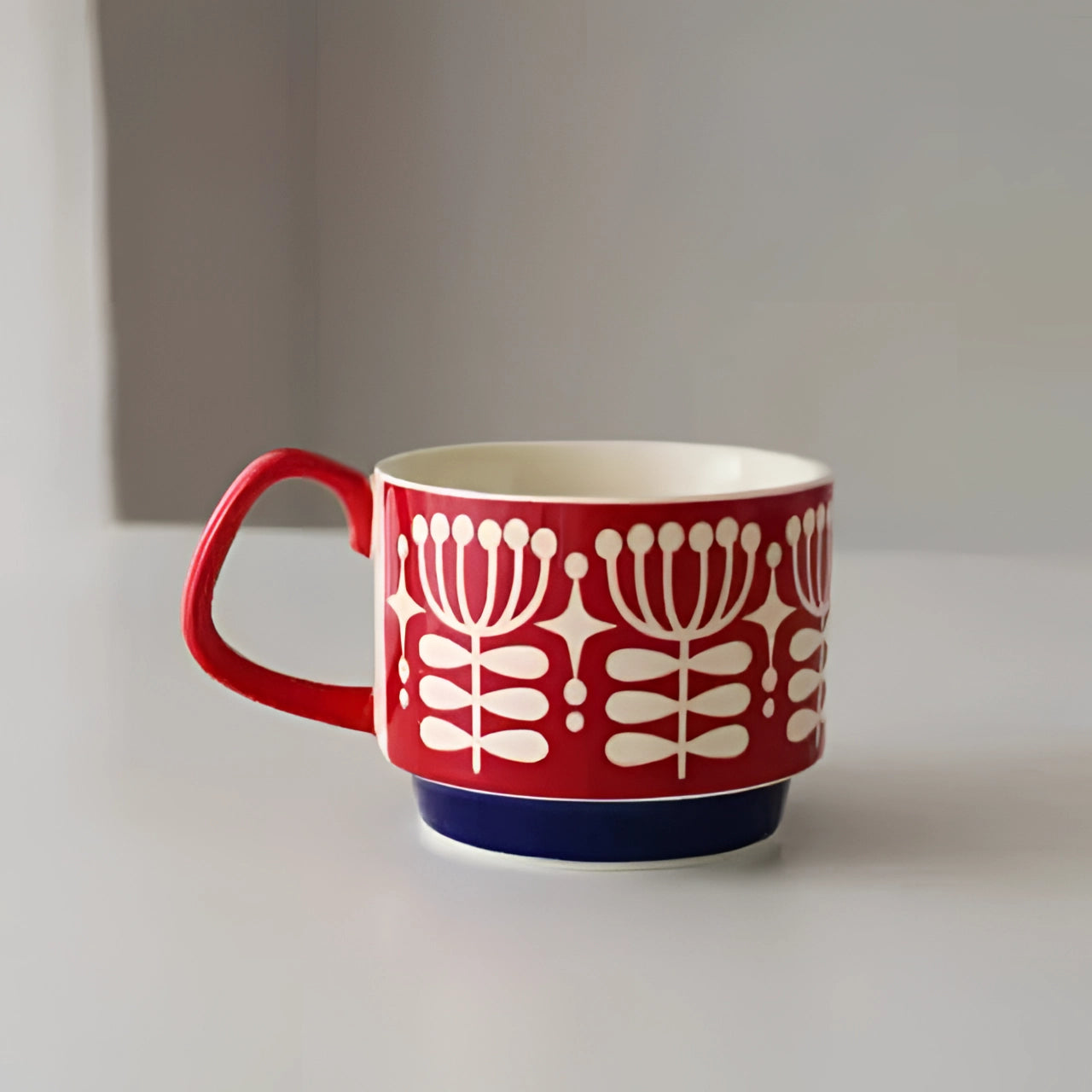 Colorful polka dot ceramic mug with a red handle and blue base, featuring white flower designs.