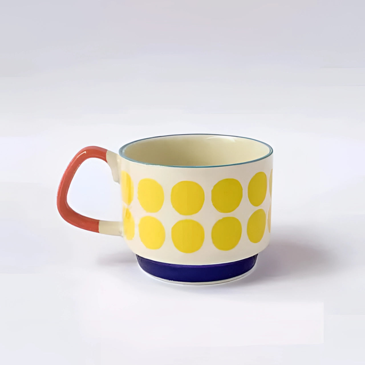 Colorful polka dot ceramic mug with red handle and blue base featuring yellow points, sitting on a matching saucer.