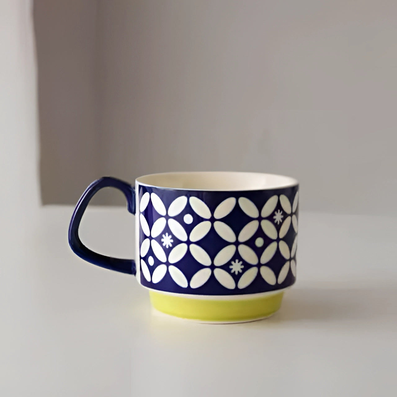 A ceramic mug featuring a colorful polka dot design with a red handle and a blue base, displaying a geometric white pattern, suitable for use as tableware and drinkware.
