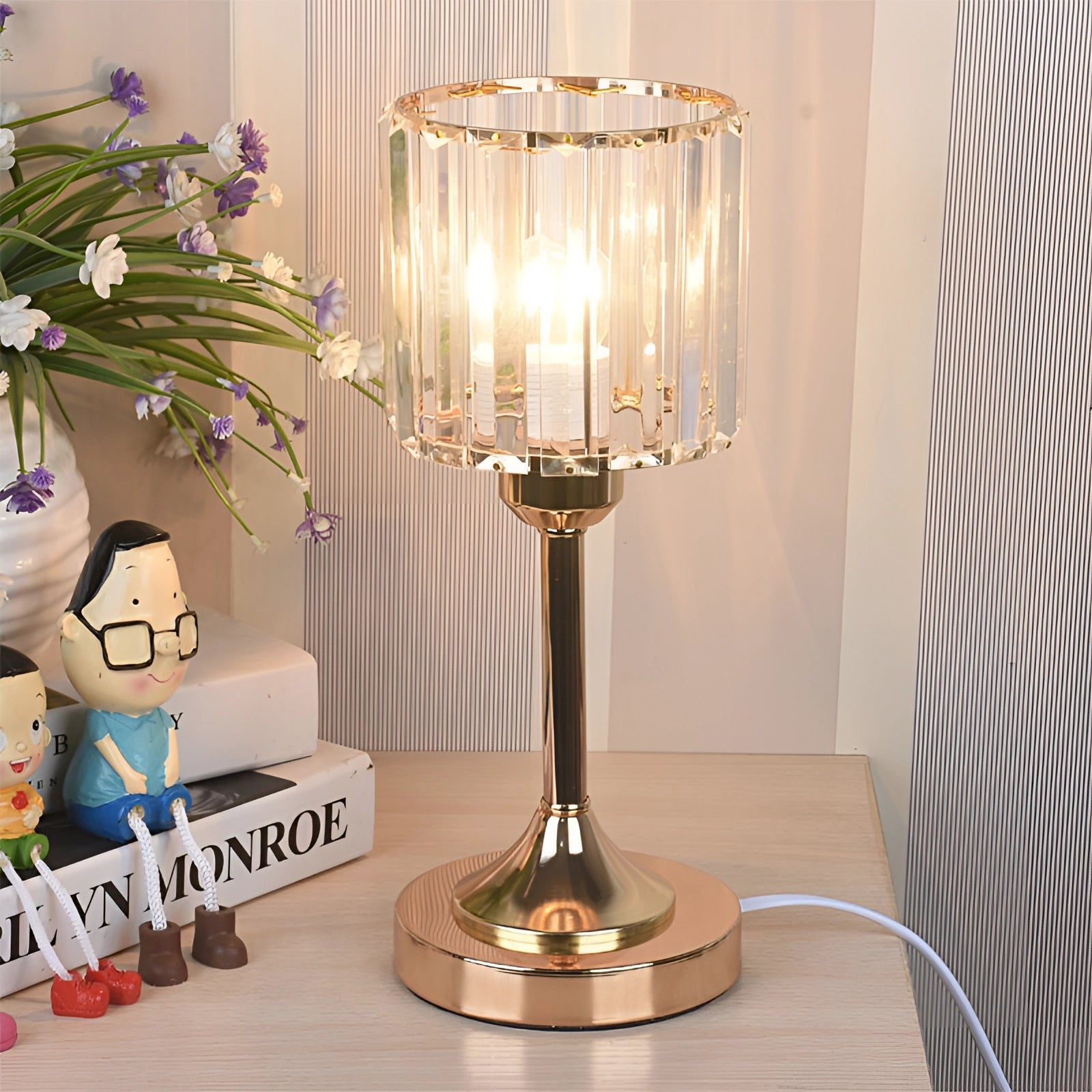 Gold finish modern round crystal brass table lamp on a wooden table, featuring a decorative design suitable for bedside or interior spaces, surrounded by minimal decor elements like plants and drinkware.