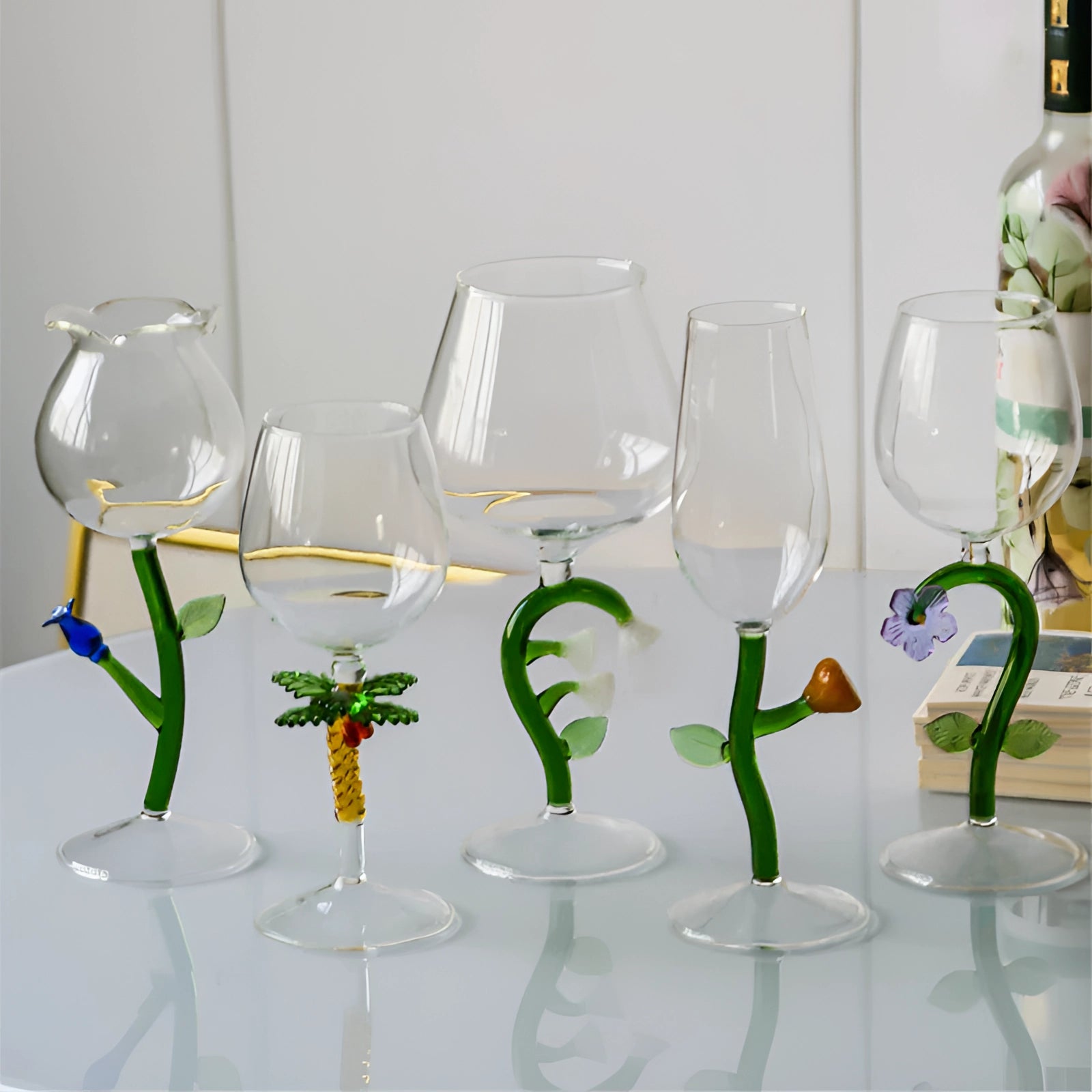 A set of decorative artistic handcrafted vineyard wine glasses displayed on a table with greenery in the background.