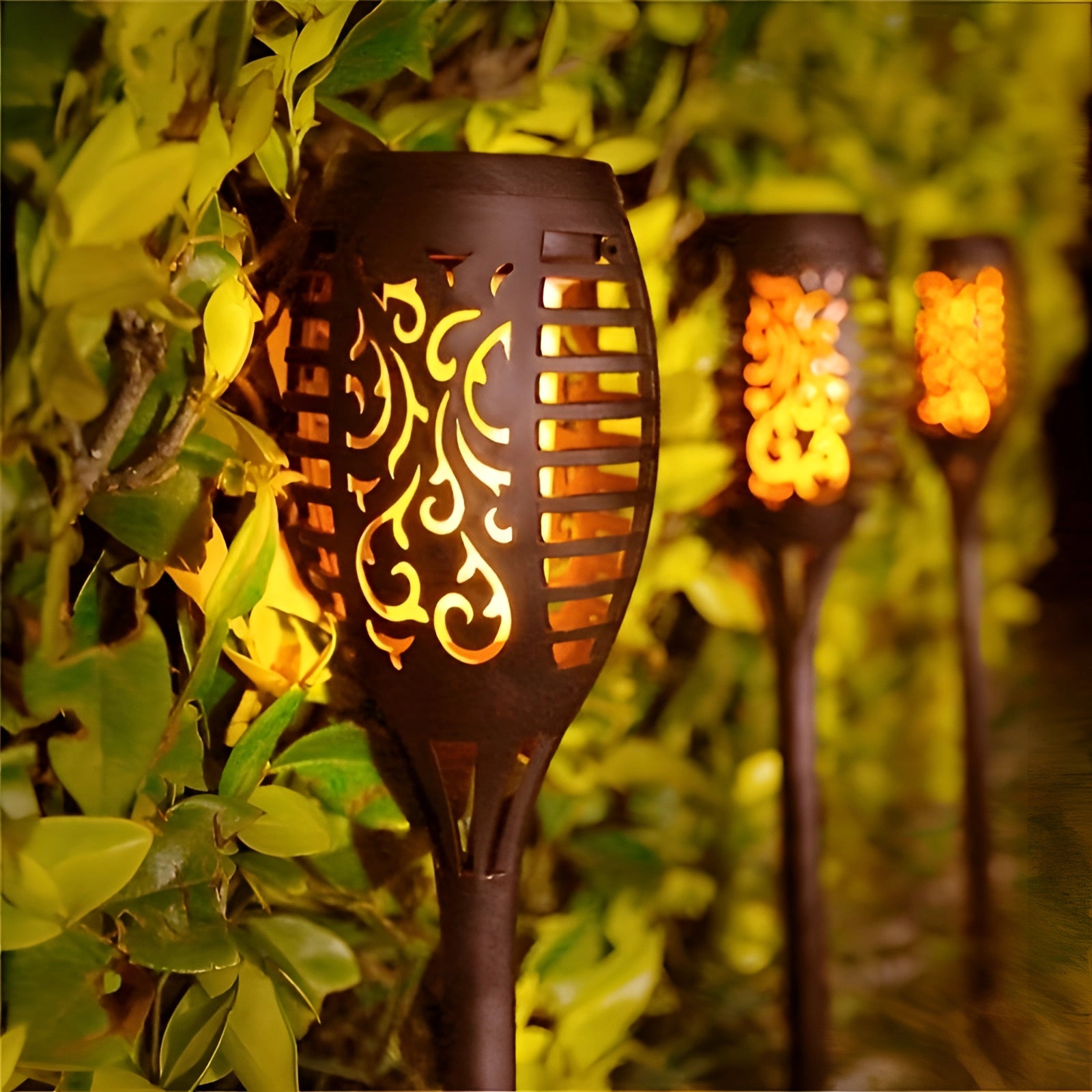 Decorative LED Solar Flame Torches illuminating a garden area at night, surrounded by plants and flowers.