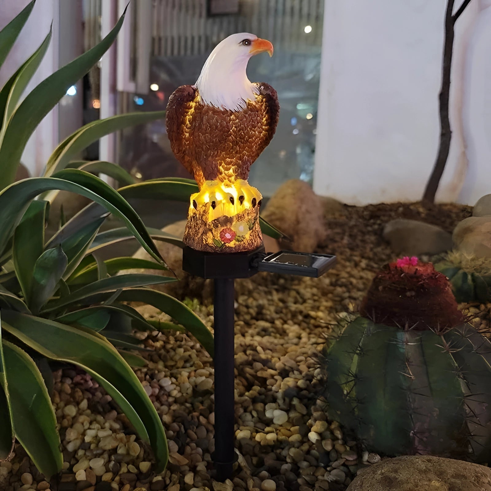 Eagle Solar LED Statue featuring a detailed eagle perched on a tree branch, illuminated by LED lights, set amidst garden plants and a flowerpot.