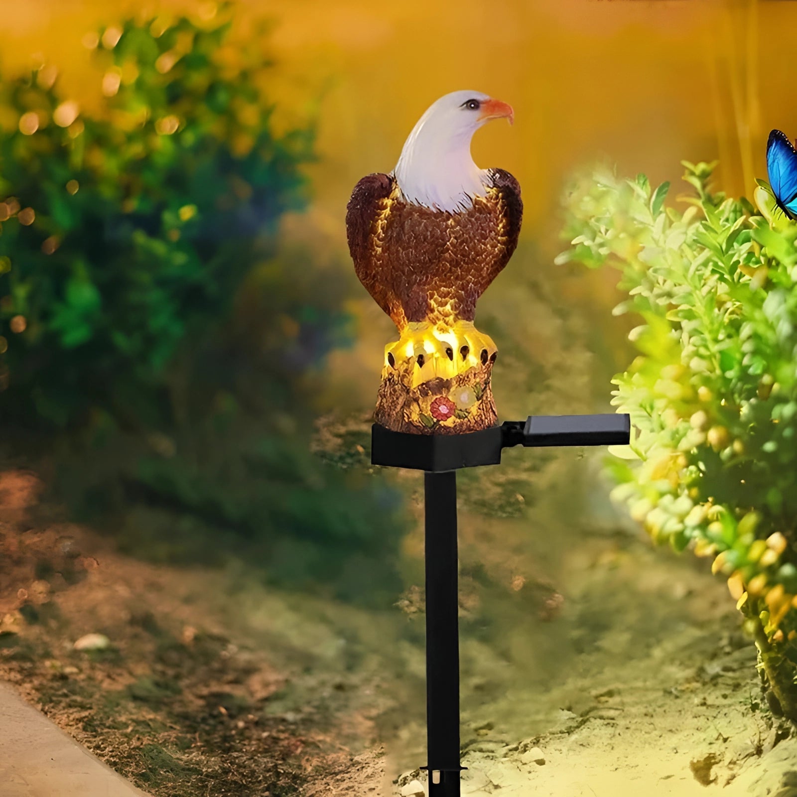 Eagle Solar LED Statue featuring a majestic eagle with detailed feathers perched in a garden setting, surrounded by grass and plants, designed as a patriotic outdoor garden light.