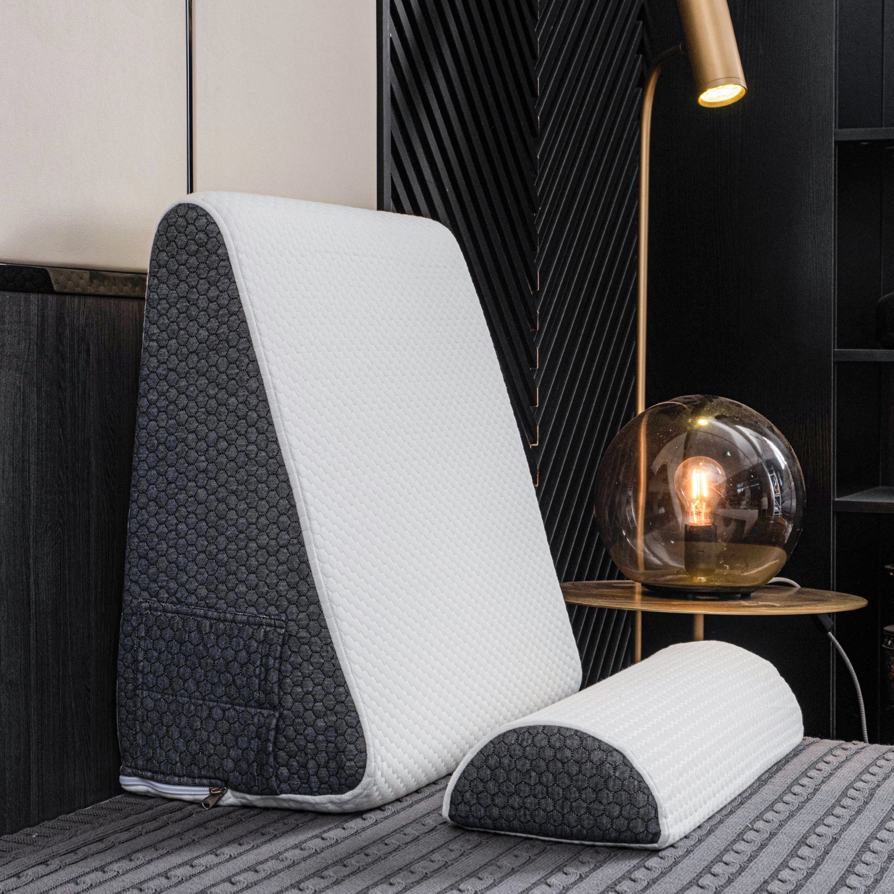 Ergonomic memory foam neck support pillow resting on a wooden floor in a cozy living room setting with a lamp and audio equipment visible in the background.