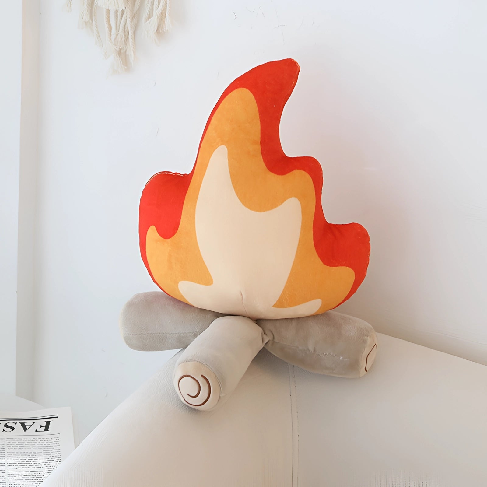 Flame-shaped plush pillow with a modern artistic design, displayed in a contemporary living room setting against a wooden background.