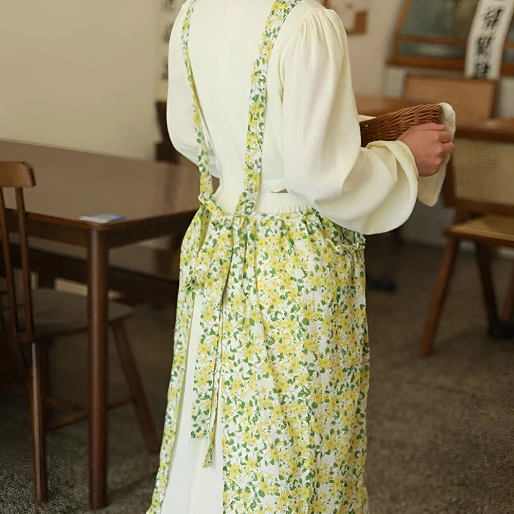 A floral cotton apron for women, featuring a vintage design with pockets, displayed on a mannequin. The apron has a full-length design covering the shoulders and extending down to the waist, showcasing a vibrant floral pattern.