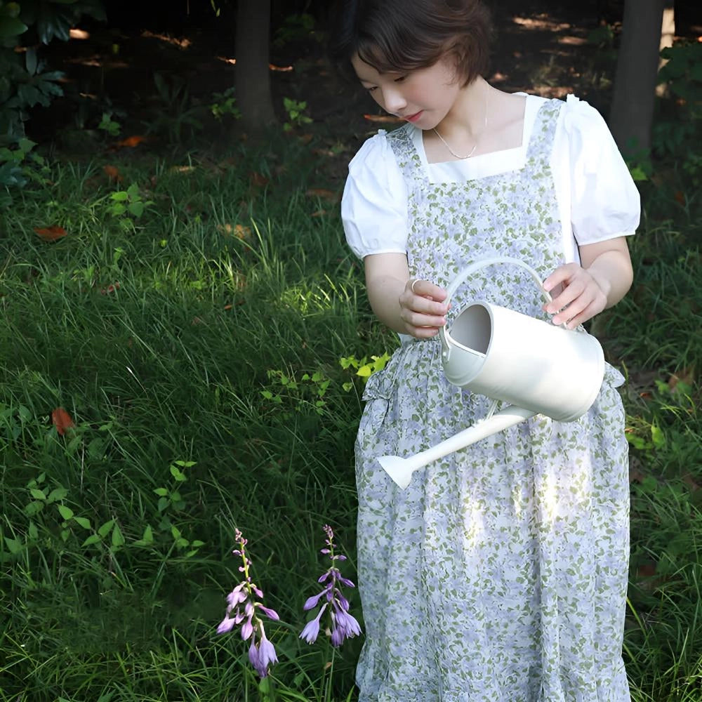 Woman wearing blue floral cotton apron with pockets, standing in a grassy meadow, smiling and enjoying nature.