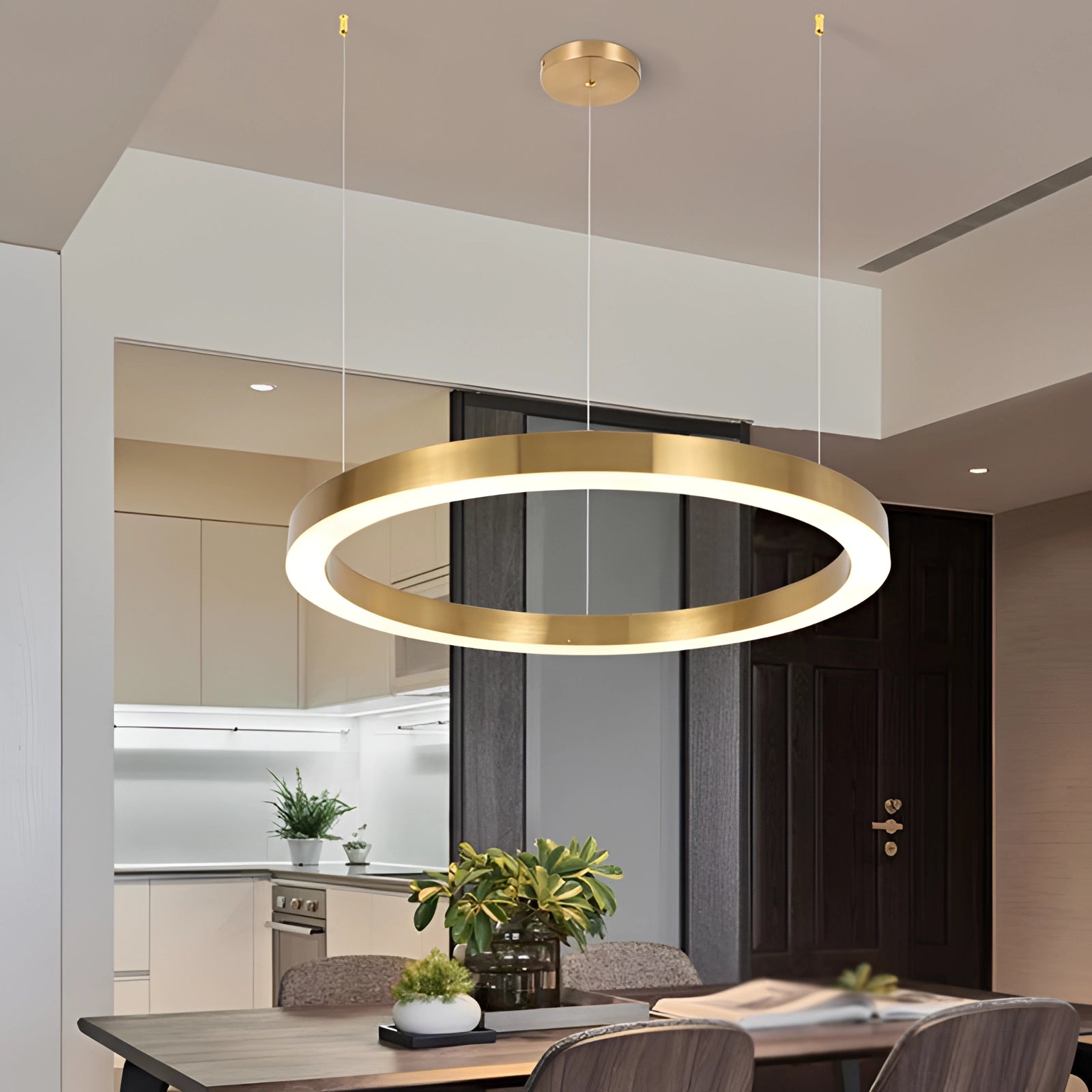 Gold circular LED chandelier with a modern minimalist design, emitting white light, hanging in a stylish living room setting featuring wooden flooring, a table, and houseplants as part of the interior decor.