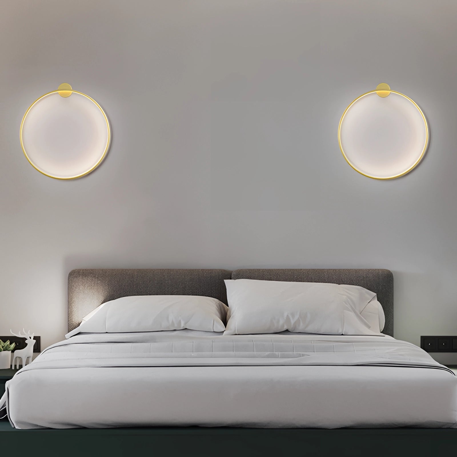 Minimalist modern gold hoop wall decor sculpture displayed in a stylish interior setting with light wood furniture, grey bed frame, and soft ambient lighting.