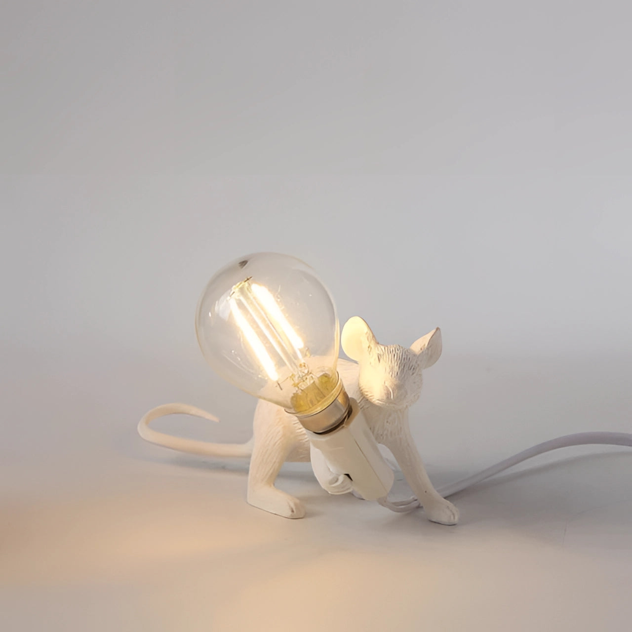 Quirky gold mouse-shaped lamp in a squatted position, designed as an eccentric desk light, featuring a detailed white finish with a long tail and artistic elements.