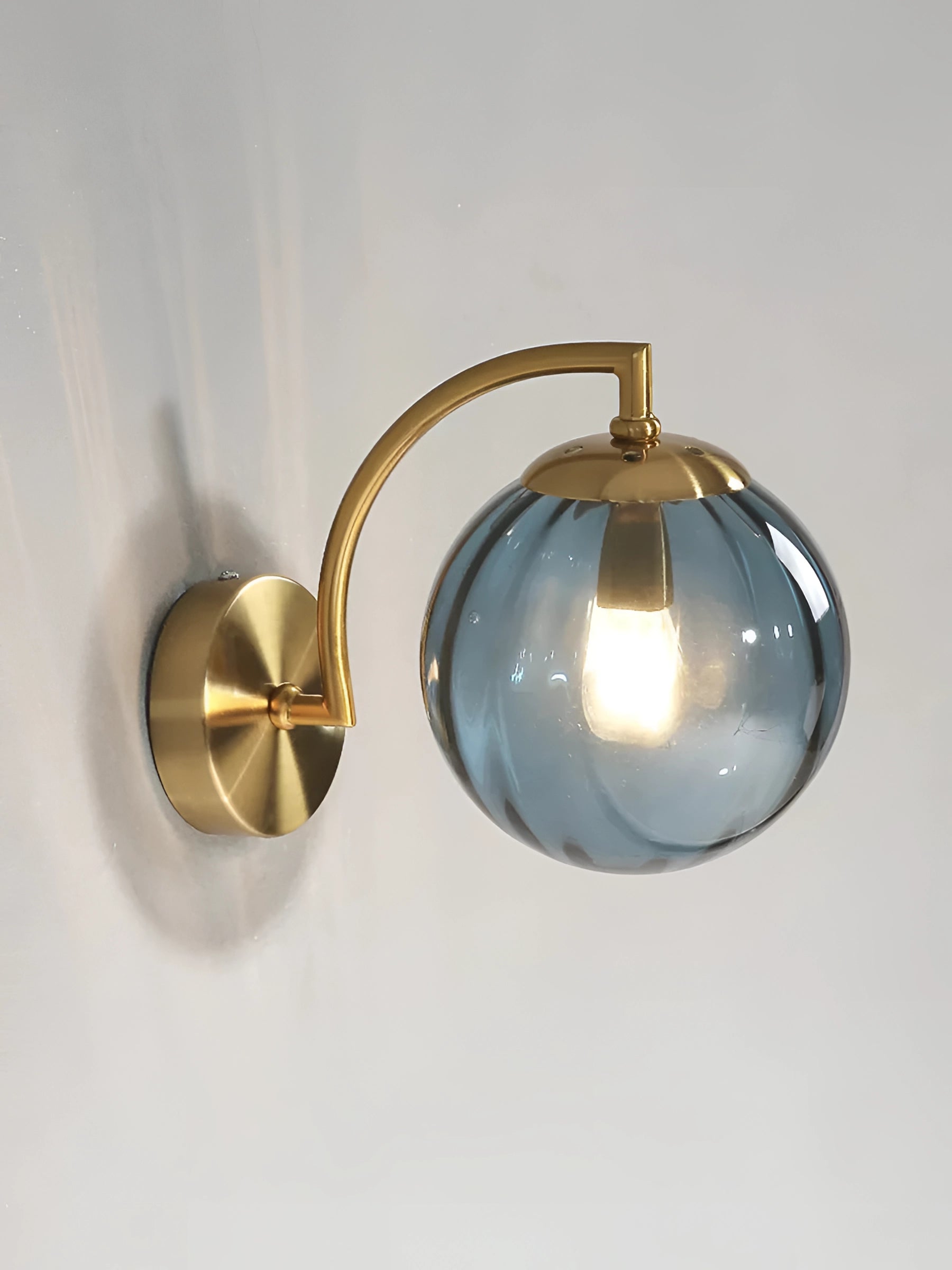 Modern gold wall sconce with ribbed glass globe and brass finish, featuring a blue accent.