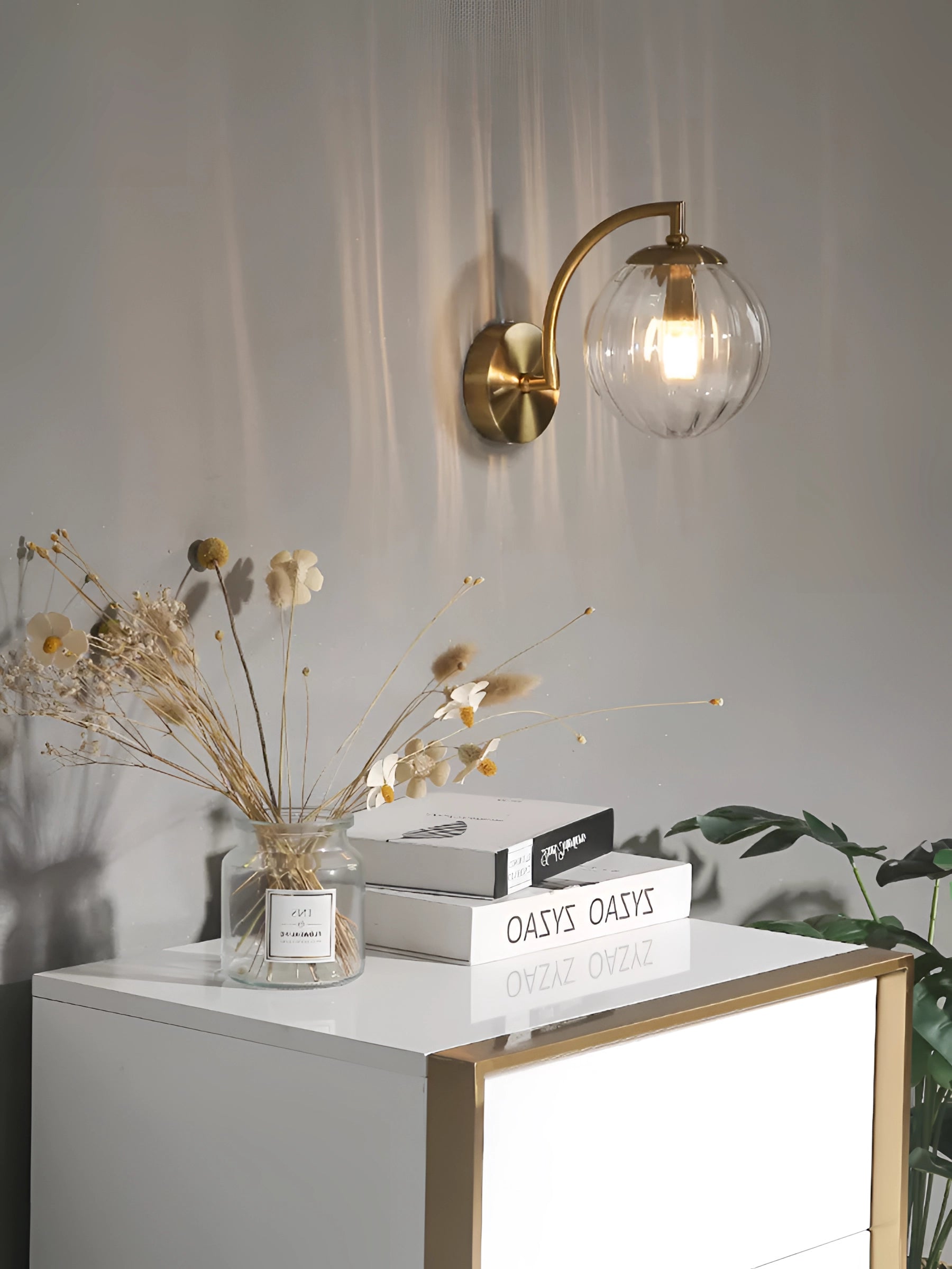 Modern gold wall sconce with ribbed glass globe, mounted on a wall above a wooden table decorated with a vase of twigs and a potted plant in a stylish interior setting.