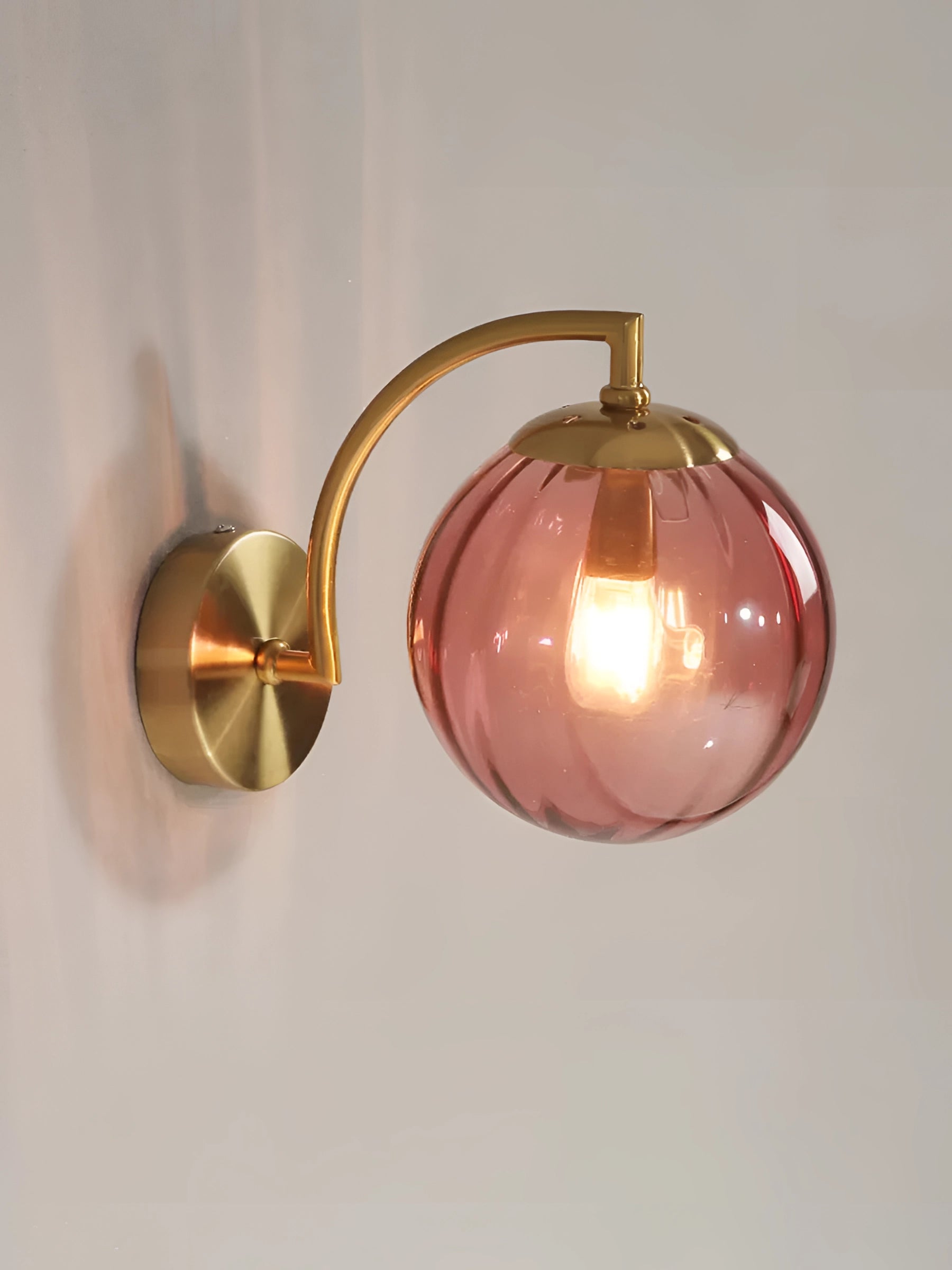 Modern gold wall sconce with ribbed glass globe, featuring a warm amber light, mounted on a wooden surface.