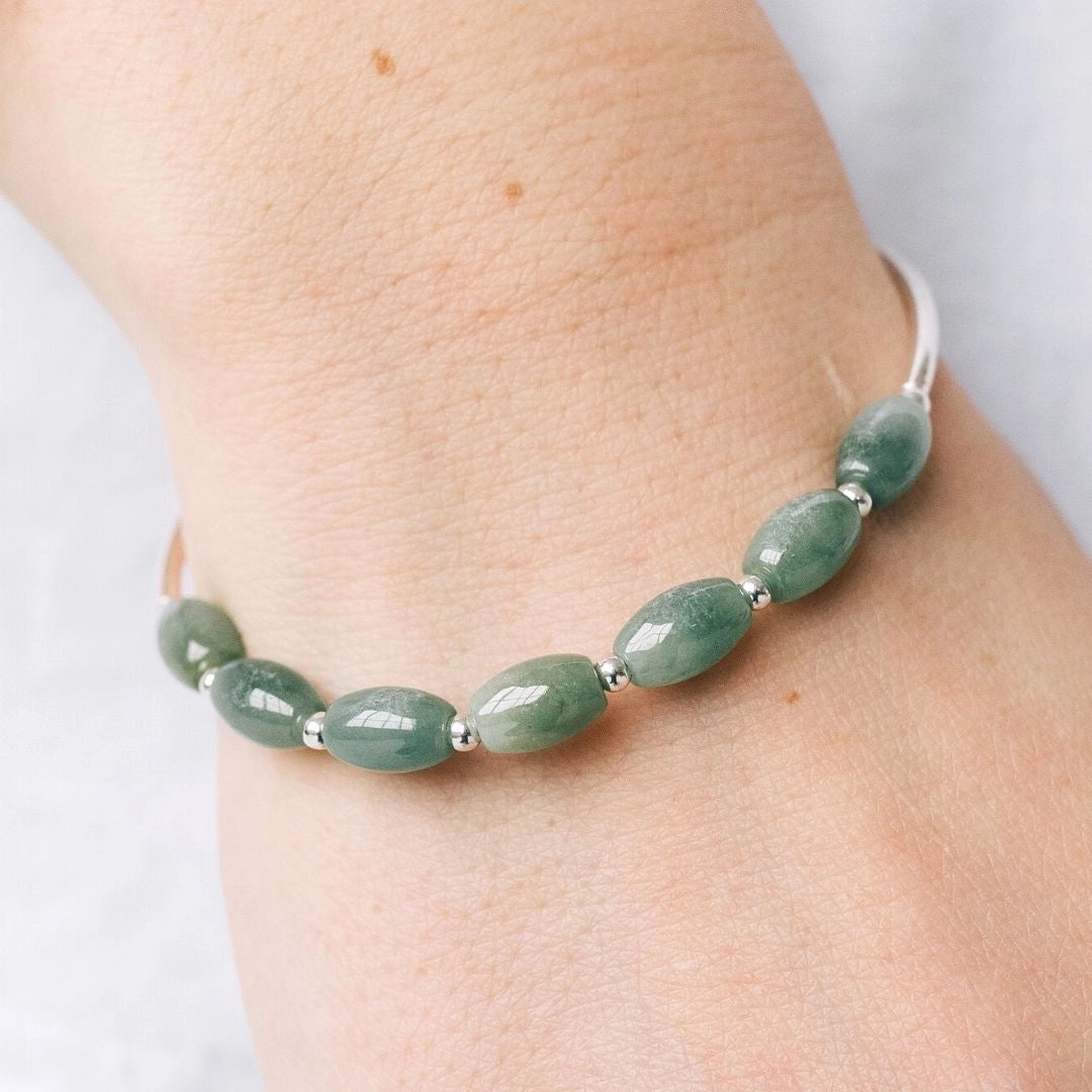 Silver bracelet featuring a natural oval green jade stone displayed on a wrist, showcasing the intricate craftsmanship and elegant design of this fine piece of jewelry.