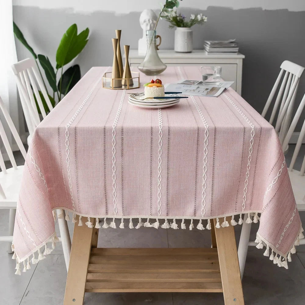 Grey linen tassel tablecloth in a Scandinavian boho design draped over a rectangular wooden table, featuring a pinkish hue and measuring 140x300cm. The table setting includes minimalistic tableware, enhancing the eco-friendly and decorative interior design ambiance.