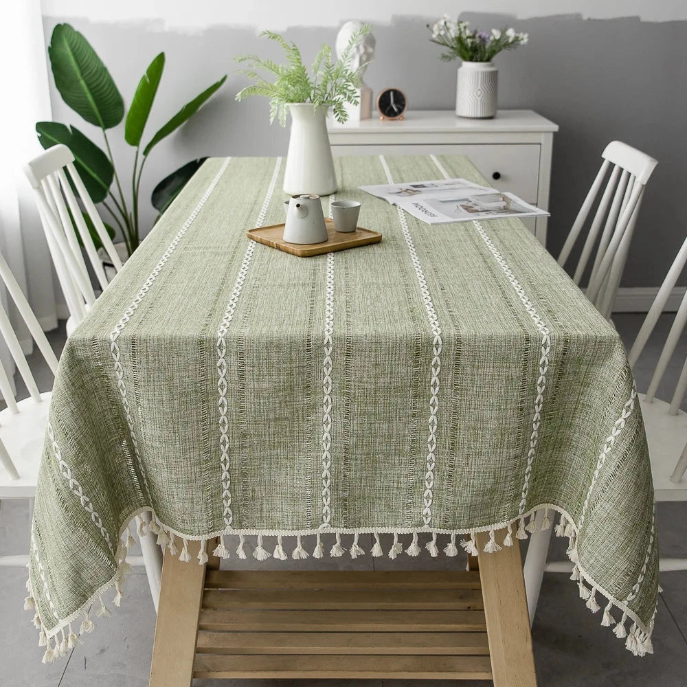 Grey linen tassel tablecloth in army green, featuring an eco-friendly Scandinavian boho design, draped over a rectangular table and adorned with decorative plants and flowers in a stylish interior setting.
