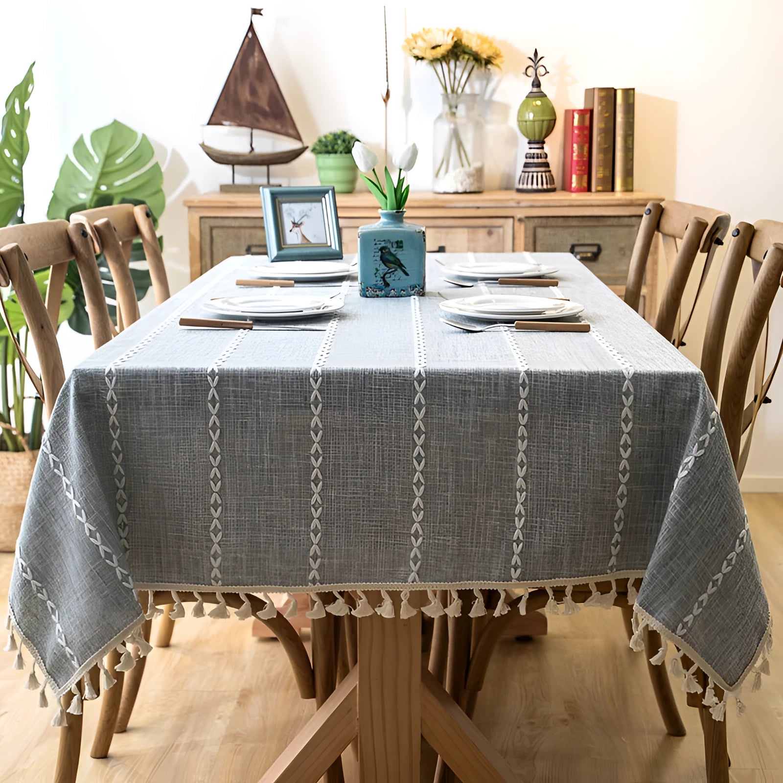 Grey linen tassel tablecloth draped over a rectangular table in a Scandinavian boho interior, with minimalistic decor including a laptop, chair, and a small plant.