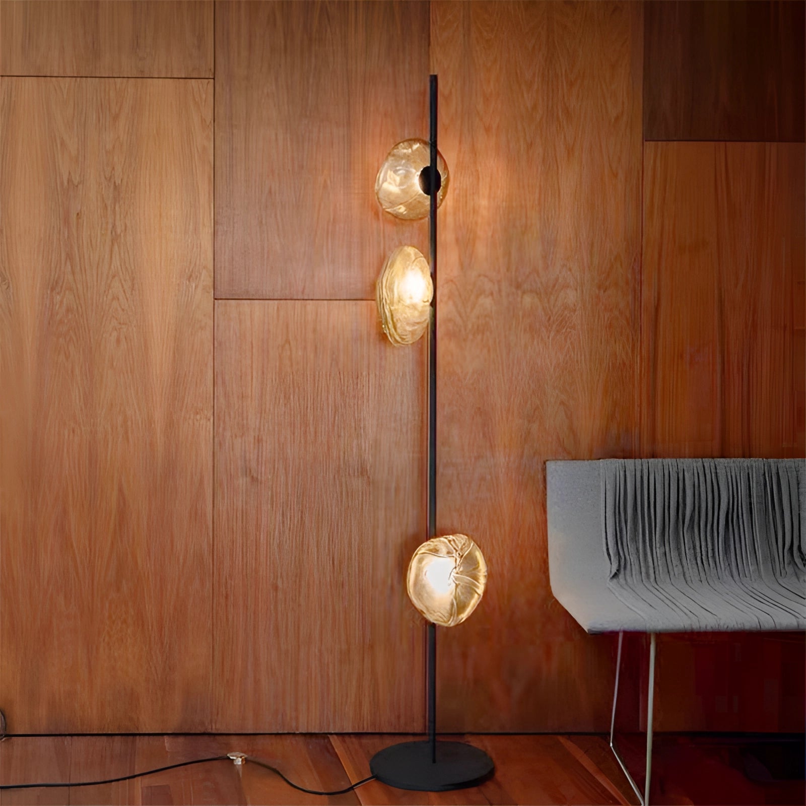 Industrial Metallic Pebble Floor Lamp with three sculptural heads in black and transparent finish, set in an interior space with wooden flooring and warm amber lighting.