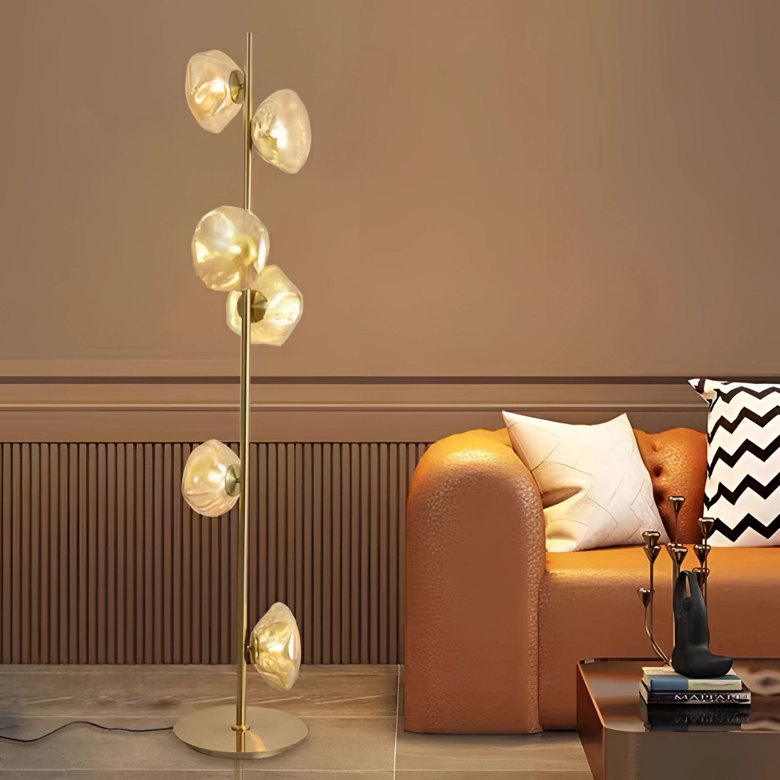 Industrial metallic pebble floor lamp with six gold and transparent heads, featuring a sculptural design, situated in an interior setting with modern decor elements like a wooden floor and a couch.