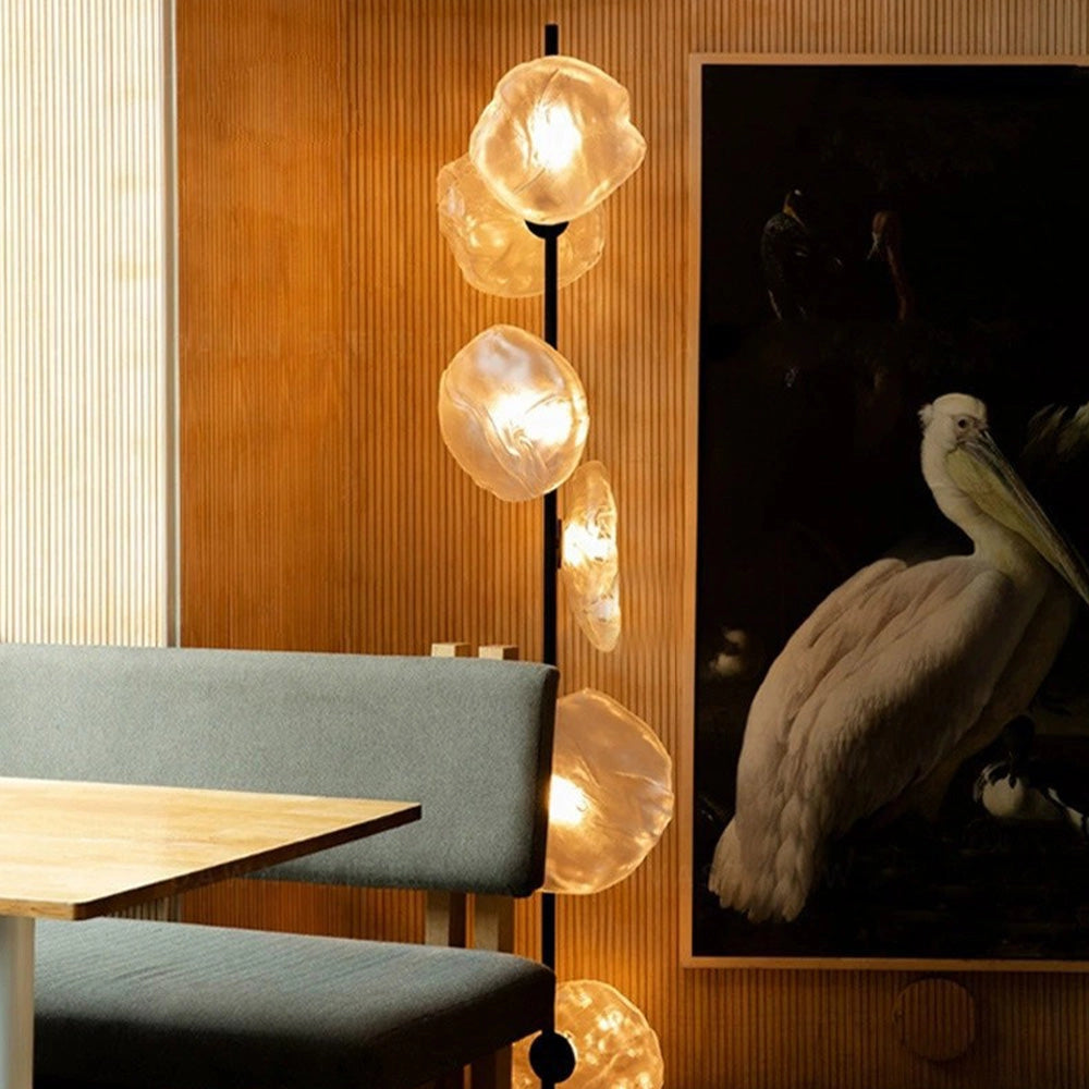 Industrial metallic pebble floor lamp with six black and transparent heads, featuring a sculptural designer style, set against a hardwood floor and light-colored wall.