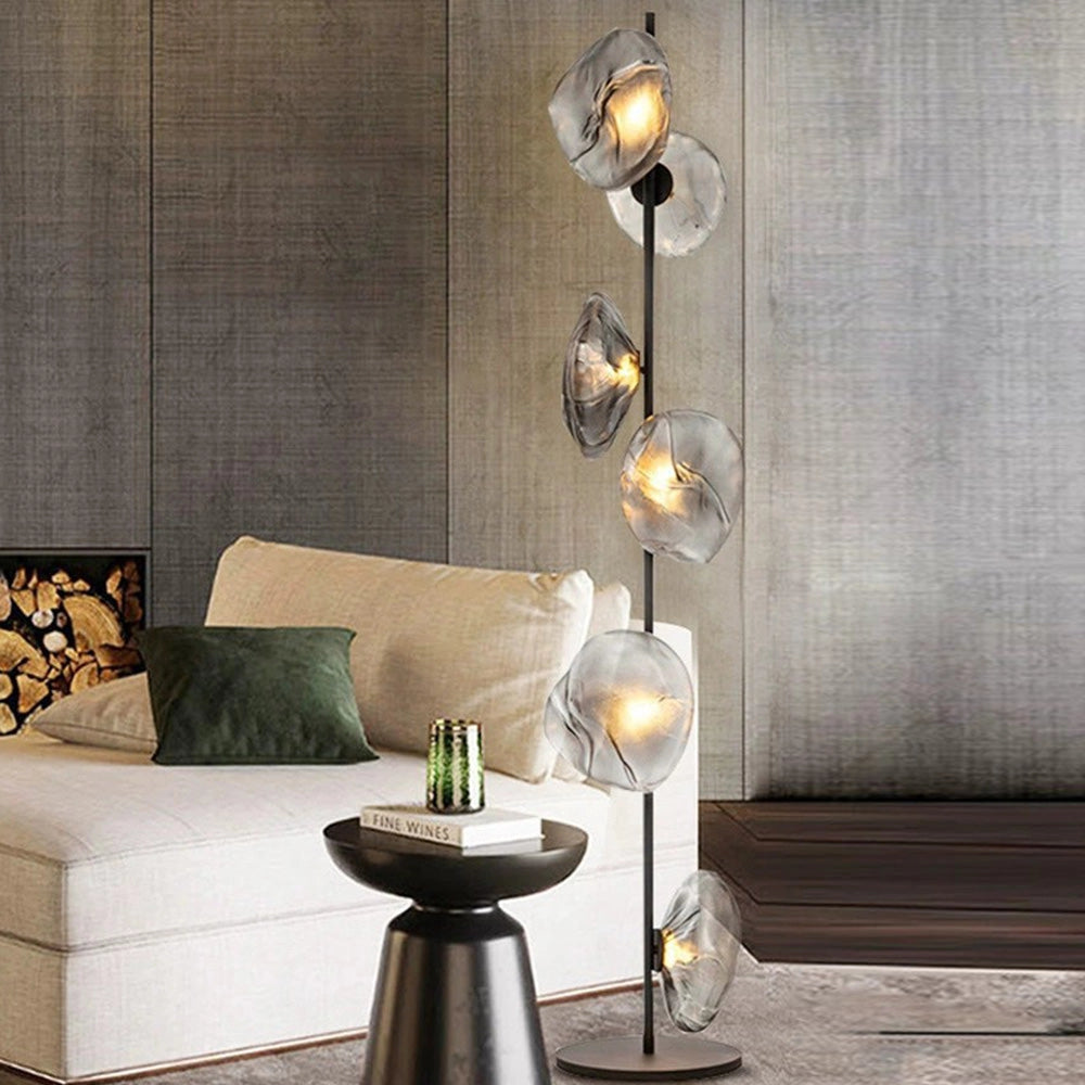 Industrial metallic pebble floor lamp with sculptural design, featuring a grey finish, placed in a modern interior setting alongside furniture like a couch and table.