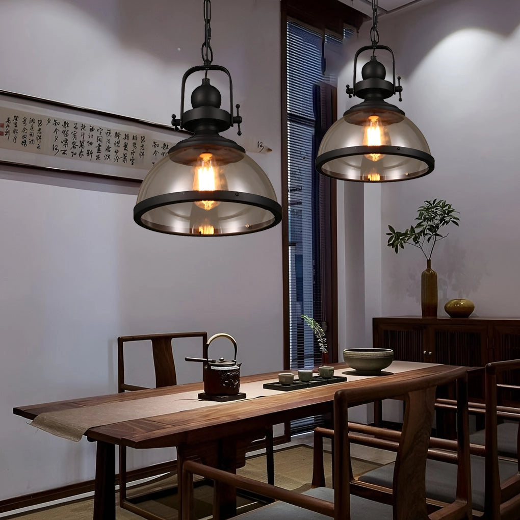 Industrial pendant lights with a rustic design featuring exposed Edison bulbs, suspended over a wooden table in a well-decorated interior setting. The scene includes additional elements like a picture frame and greenery to enhance the cozy ambiance.