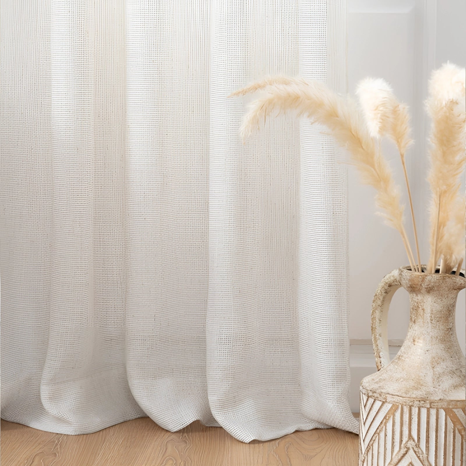 Ivory sheer curtains with an elegant linen texture, partially drawn on a wooden rod, allowing soft natural light to filter into the living room. The curtains exhibit a delicate, minimalist design complementing a neutral beige color scheme.