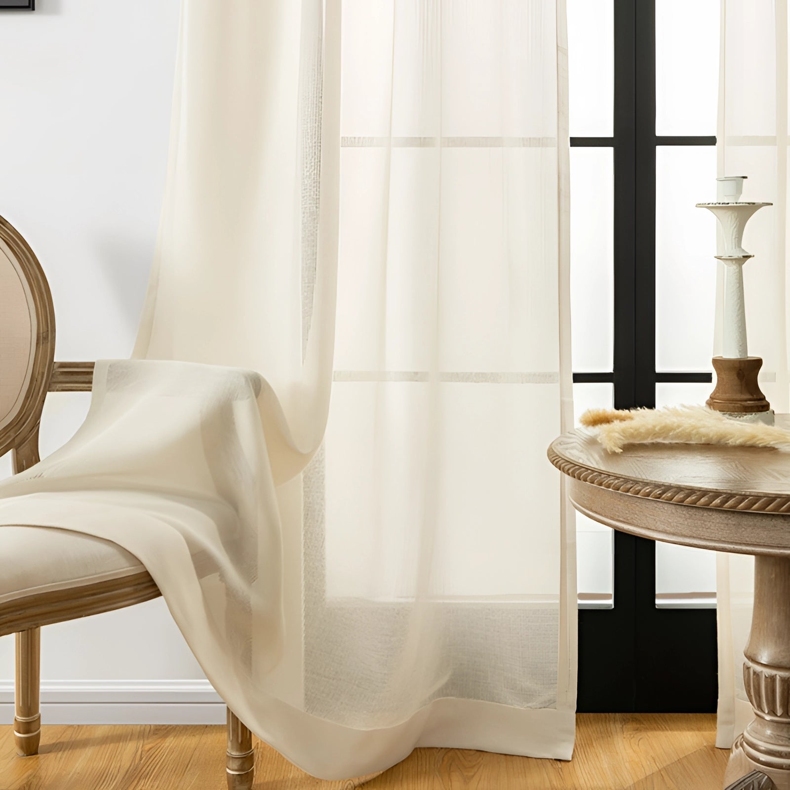 Ivory sheer curtains hanging in a living room, with elegant linen drapes showcasing their translucent texture. The room features wooden furniture and a beige color palette, creating a comfortable and stylish interior design.