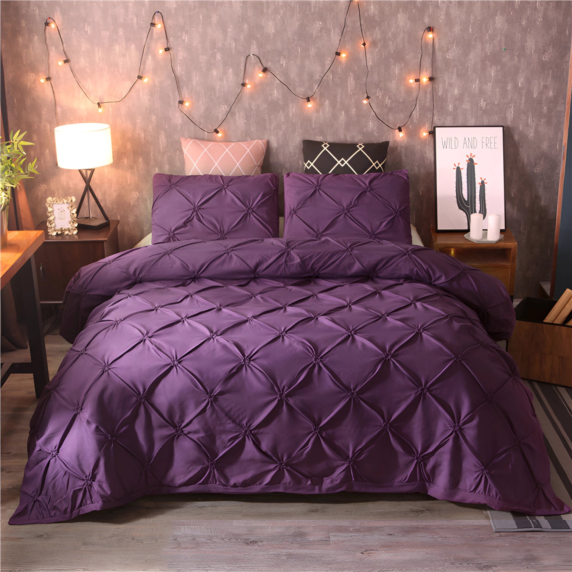 Luxurious black pinch pleat comforter on a bed in a modern bedroom setting, featuring a rich purple color. The scene includes a grey bed frame, a wooden bedside table with a lamp, and decorative elements like a flowerpot, emphasizing a cozy and stylish interior design.