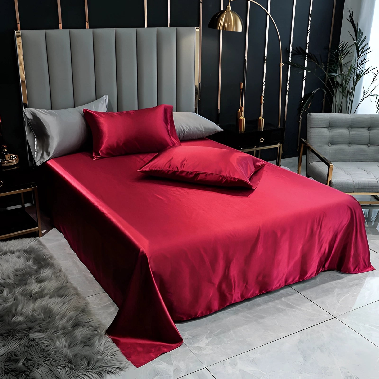 Luxury black silk bedding set with elegant satin bed sheets and duvet cover in a deep red color, perfectly arranged on a wooden bed frame in a stylishly designed bedroom. The bedding exudes comfort and sophistication, complementing the interior design with its luxurious texture and rich hue. Room features a smooth wooden floor, enhancing the overall elegant ambiance.