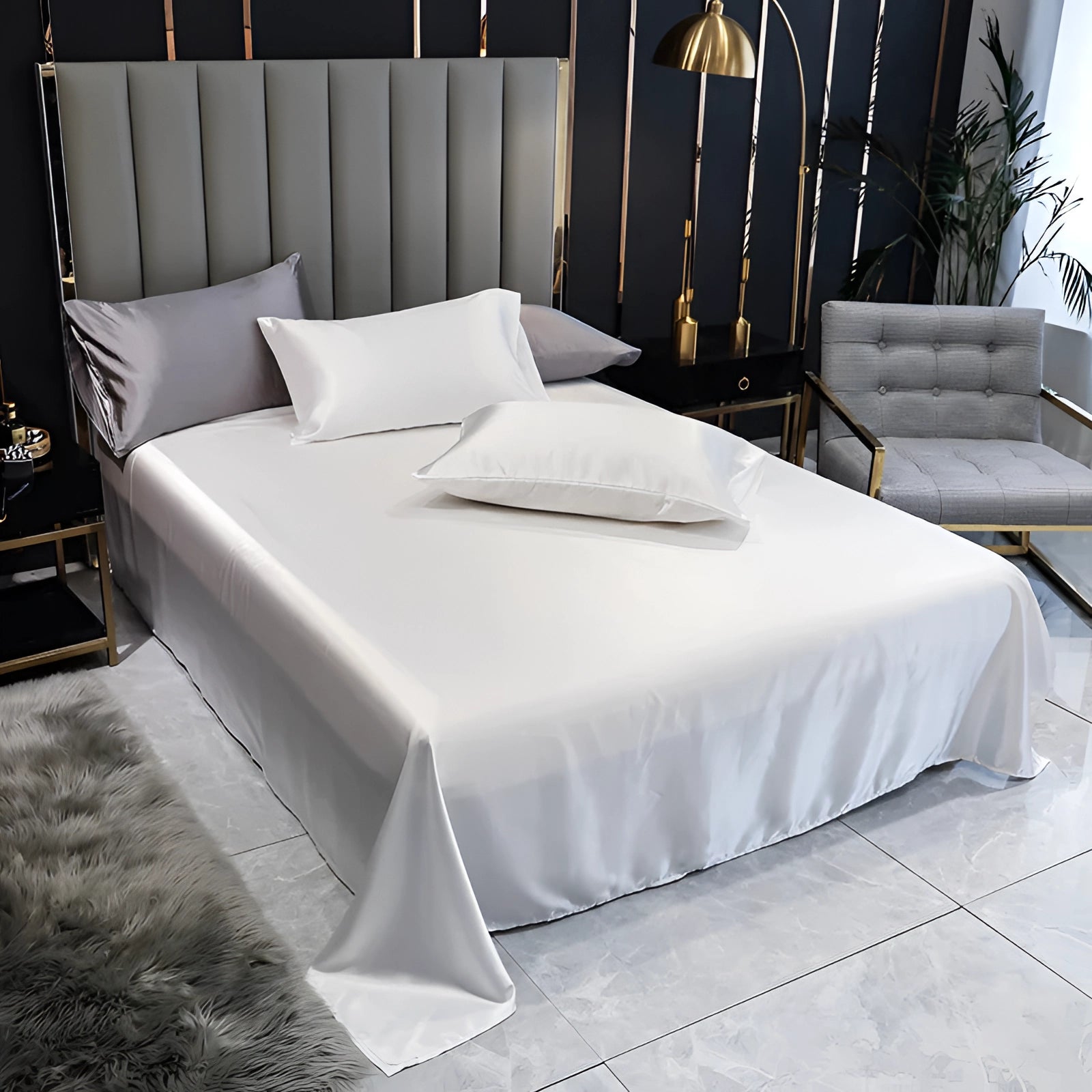 Luxury white satin bedding set with elegant silk sheets and duvet cover, displayed on a bed with a black frame, situated in a stylishly designed bedroom interior featuring wood and grey accents.