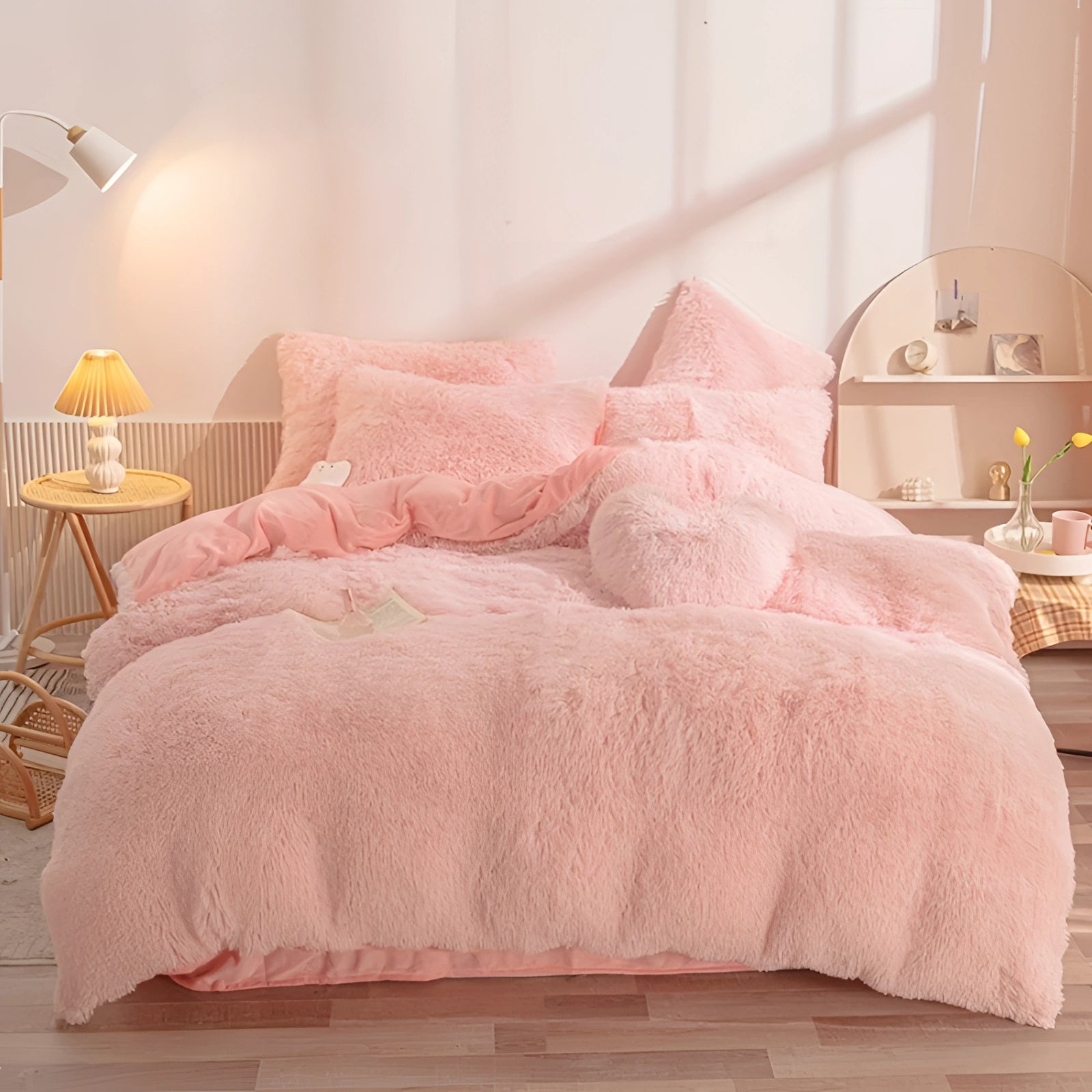 Luxury light pink faux fur bedding set on a superking bed with plush comforter and matching shams, surrounded by a wooden bed frame and hardwood flooring, complemented by a cozy atmosphere with a bedside lamp.
