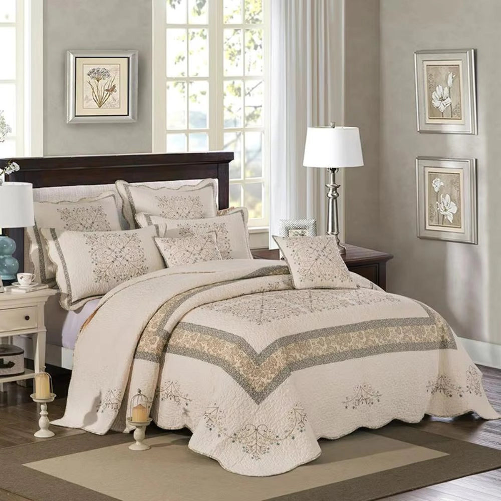 Luxurious floral quilt set with embroidered pillowcase and scalloped edges displayed on a super king bed, featuring a wooden bed frame, a lamp on a bedside table, and a window providing natural light in a comfortable bedroom setting.